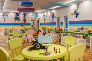 Bunte Spielecke im Delphin BE Grand Resort mit Tischen, Stühlen, Spielzeug und Wandmalereien.