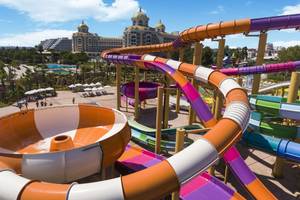 Blick auf die bunten Wasserrutschen im Delphin BE Grand Resort mit Pool und Liegen im Hintergrund.