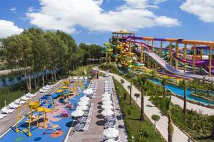 Wasserpark mit bunten Rutschen und Liegen im Delphin BE Grand Resort, umgeben von Grün und Himmel.