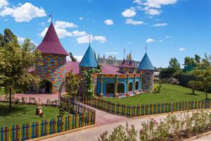 Bunte Architektur des Delphin BE Grand Resort mit Türmen, Garten und Spielplatz, unter blauem Himmel.