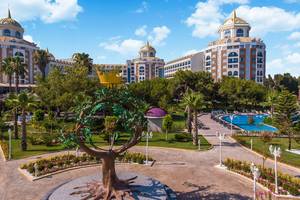 Luxuriöses Delphin BE Grand Resort mit Palmen, Gärten und einer Statue in der Vorderansicht unter klarem Himmel.