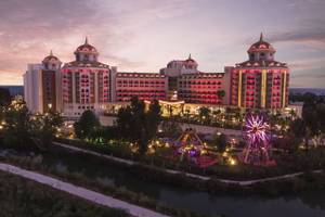 Hotel Delphin BE Grand Resort bei Dämmerung, beleuchtet, mit Riesenrad und Spielplatz im Vordergrund.