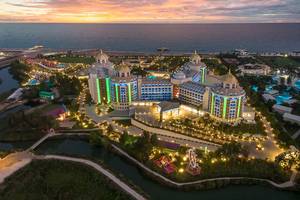Luftaufnahme des Delphin BE Grand Resort mit bunten Lichtern und Blick auf das Meer bei Sonnenuntergang.