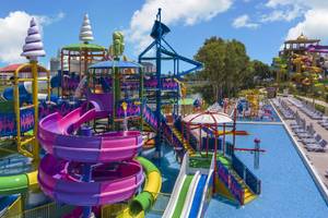 Wasserpark mit bunten Rutschen und Pools im Delphin BE Grand Resort, umgeben von Sonnenliegen und grüner Landschaft.