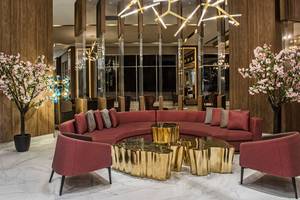 Modernes Hotel-Lobby im Delphin BE Grand Resort mit rotem Sofa, goldenen Tischen und blühenden Bäumen.