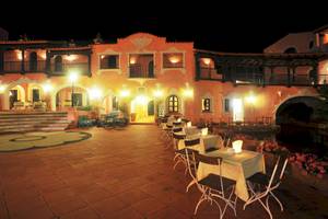 Abendansicht des Bagaglino I Giardini di Porto Cervo Hotels mit beleuchteten Außenbereichen und Tischen.