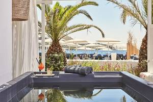 Poolbereich des Mykonos Ammos Hotels mit Blick auf die Palmen, Sonnenschirme und das Meer.