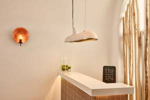 Rezeptionsbereich des Mykonos Ammos Hotels mit einer Wandlampe, einem Glasgefäß mit Früchten und einem Schild mit der Aufschrift 'the spa'.