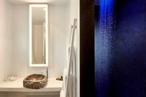 Badezimmer im Mykonos Ammos Hotel mit Steinwaschbecken, Spiegel und blauer Regendusche