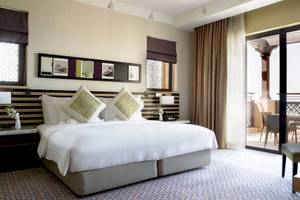 Hotelzimmer im Jumeirah Mina A'Salam mit großem Bett, Balkon und Gartenblick.