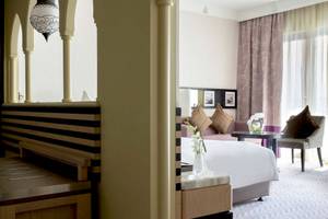 Innenansicht des Jumeirah Mina A'Salam Hotelzimmers mit Bett, Sitzbereich und Fenstern.