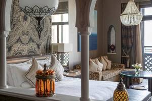 Luxuriöses Hotelzimmer im Jumeirah Mina A'Salam mit üppigen Kissen, eleganten Kronleuchtern und einem Blick auf das Meer.