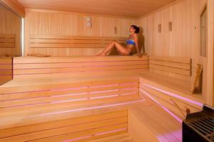 Frau sitzt in einem Holzsauna mit blauen und rosa Lichtern