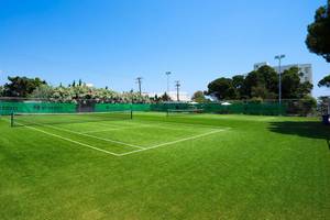 Tennisplatz auf dem Apollo Beach Hotelgelände, mit einem geschlossenen Schirm und grünem Rasen.