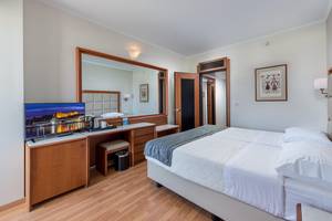 Innenansicht eines Hotelzimmers im Apollo Beach Hotel mit Fernseher, Schreibtisch und Bett.