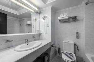 Badezimmer im Apollo Beach Hotel mit Waschbecken, Spiegel, Toilette und Handtüchern.