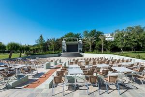 Apollo Beach Hotel mit Outdoor-Veranstaltungsort, vielen Tischen und Stühlen, Bühne und Bäumen im Hintergrund.