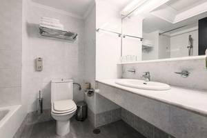 Badezimmer im Apollo Beach Hotel mit weißer Fliesenwand, Toilette, Waschbecken und Spiegel.