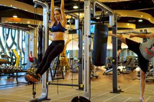 Fitnesstraining im Fitnessstudio mit einer Frau, die an einem Zuggerät hängt, und einem Mann, der einen Kickboxschlag ausführt.
