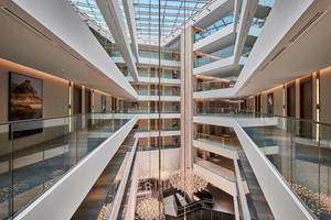 Innenansicht des Mysk Al Mouj Hotels mit Atrium, mehreren Ebenen und großen Glasfenstern.