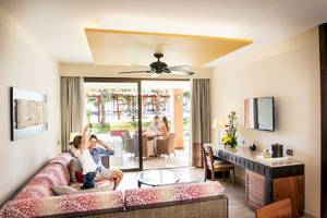 Innenansicht einer Suite im Barcelo Maya Grand Resort mit zwei Personen, die draußen sitzen und ein Mädchen, das die Hände hebt.