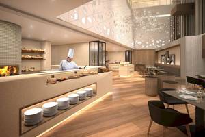 Innenansicht des Mysk Al Mouj Hotels mit einem Koch, der Speisen auf einem Buffet zubereitet.