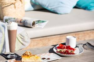 Frühstückstisch im Universal Hotel Neptuno mit Kuchen und Getränken auf einer Terrasse.