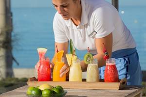 Eine Mitarbeiterin des Universal Hotel Neptuno serviert Cocktails an einem Tisch mit Blick auf das Meer.