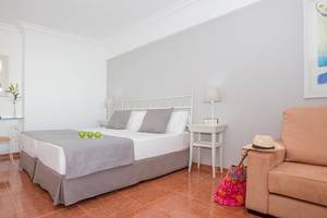 Schlafzimmer im Universal Hotel Neptuno mit weißem Bett, grauen Kissen, grünen Äpfeln, zwei Nachttischen, Tischlampe und einem Spiegel.