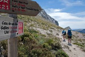 Wanderer auf einem Bergpfad mit einem Wegweiser, der Casa de neu den Gallieu und Lluc anzeigt