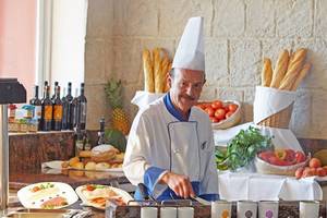 Koch in der Universal Hotel Neptuno Küche mit vorbereiteten Gerichten und Zutaten im Hintergrund.