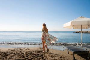 Eine Frau am Strand des Royal Apollonia Beach Hotels mit einem weißen Sonnenschirm im Hintergrund.