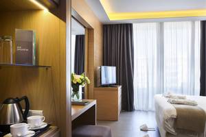 Innenansicht eines Zimmers im Royal Apollonia Beach Hotel mit Bett, Schreibtisch und Fernseher.