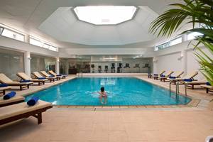 Ein Schwimmer im Innenpool des Royal Apollonia Beach Hotels, umgeben von Liegestühlen und Fitnessgeräten.