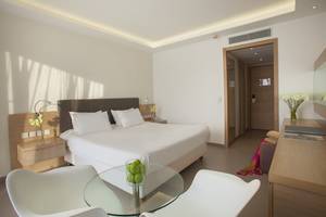 Weißes Zimmer im Royal Apollonia Beach Hotel mit Doppelbett, Tisch und Stühlen.