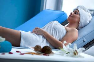 Eine Frau entspannt sich im Spa-Bereich des Seaside Los Jameos, mit einem Handtuch auf dem Kopf und auf einem blauen Liegestuhl.