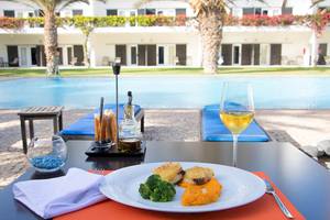 Gedeckter Tisch am Pool mit Essen, Wein und Hotel Dunas De Sal im Hintergrund.