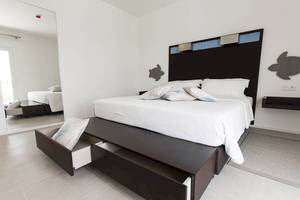 Schlafzimmer im Dunas De Sal Hotel mit weißem Bett und schwarzen Nachttischen.