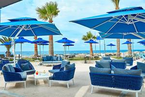Loungebereich des Mare Ayia Napa Hotels mit blauen Sonnenschirmen und Möbeln am Meer.