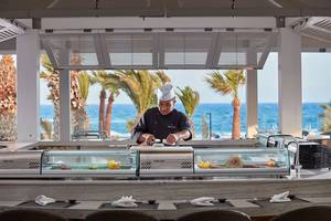 Ein Koch bereitet Sushi in einer Glasfalle im Mare Ayia Napa Hotel zu, mit Blick auf das Meer.