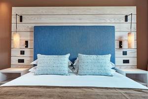 Bett im Mare Ayia Napa Hotelzimmer mit blauem Kopfteil und weißen Nachttischen.