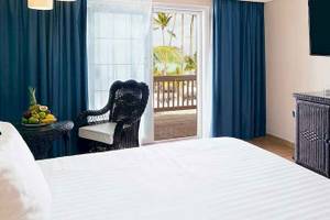 Hotelzimmer im Barcelo Bavaro Beach mit Bett, Früchten auf dem Tisch und offenem Balkon.