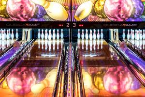 Eine Bowlingbahn mit bunten Bowlingkugeln und Kegeln, bunt beleuchtet.