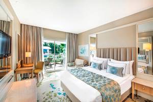 Ein elegantes Hotelzimmer im Titanic Deluxe Lara Hotel mit einem großen Bett, einem Balkon und einer Aussicht auf den Garten.