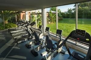 Fitnesscenter mit mehreren Laufbändern und Blick auf eine Wiese im Titanic Deluxe Lara Hotel.