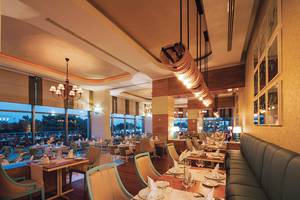 Innenraum des Restaurants des Titanic Deluxe Lara Hotels mit elegant eingerichteten Tischen und Stühlen.