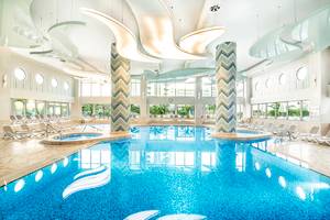 Ein großer Innenpool im Titanic Deluxe Lara Hotel mit Loungeliegen und modernen Leuchten.