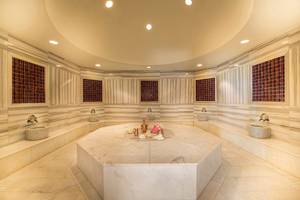 Innenbereich der Sauna im Titanic Deluxe Lara Hotel mit acht Sitzbänken und einem zentralen Tisch.