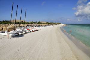 Foto einer weißen Sandstrand mit mehreren Booten und Strohhüten