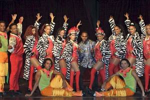 Eine Gruppe von Tänzern und Tänzerinnen in bunten Kostümen, die eine Show auf der Bühne des Grand Palladium Bavaro Suites Resort & Spa veranstalten.
